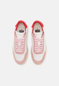Paire de baskets blanches avec des superpositions en daim rose, des lacets roses et des languettes de talon rouges, arborant la marque Copenhagen Studios sur les languettes.