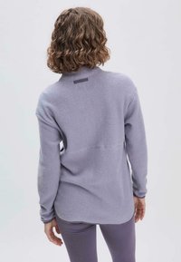 Helllila Fleece-Oberteil mit hohem Kragen, langen Ärmeln und einer Rückennaht-Detail. Weicher Stoff und lockere Passform, getragen mit passenden Hosen.