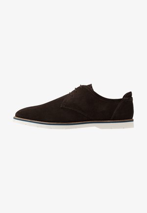 Chaussure à lacets pour homme en daim marron foncé avec semelle en caoutchouc blanche et bordure bleue, profil latéral sur fond blanc.