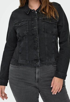 Person iført en tætsiddende sort denimjakke med knaplukning foran og matchende sorte denimjeans.