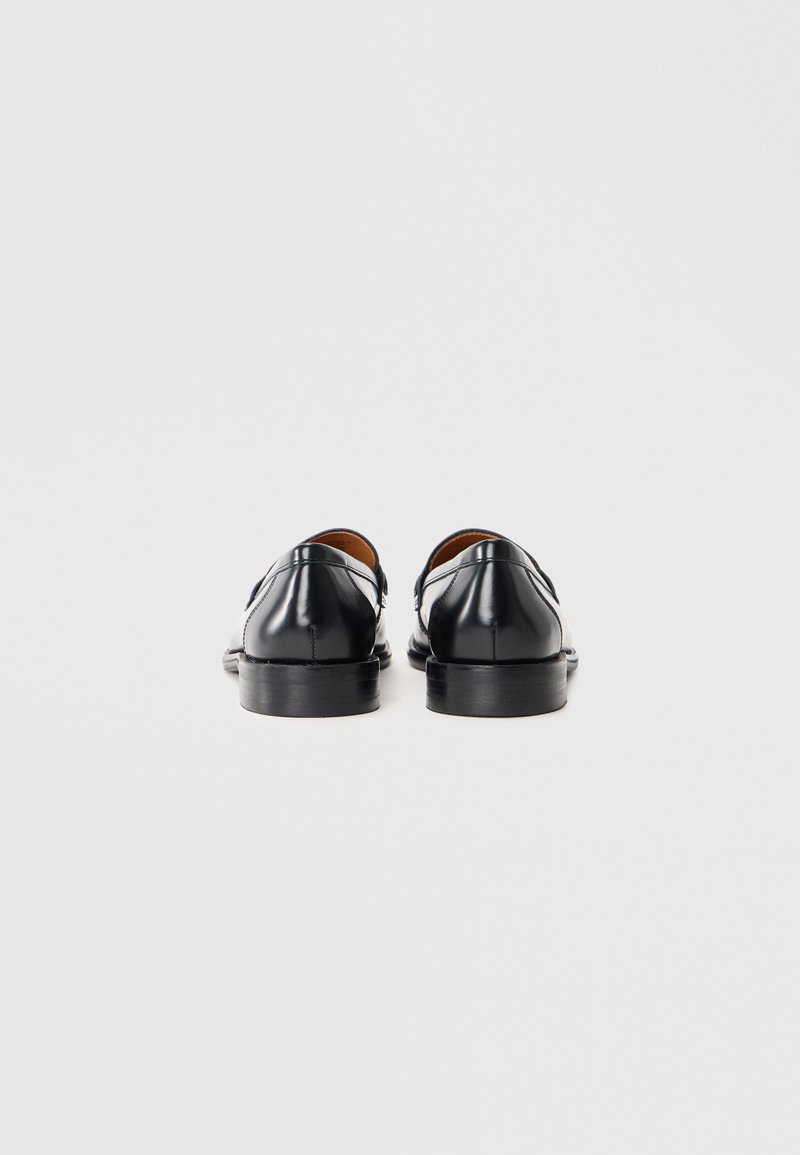 Scarpe in pelle nera con finitura lucida, punta tondeggiante e suola nera sottile, caratterizzate da cuciture minime e senza decorazioni.