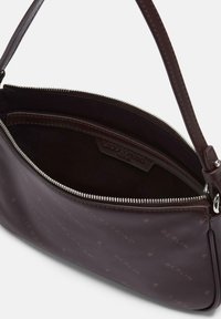Ciemnobrązowa skórzana torba na ramię z srebrnym suwakiem, wytłoczonym logo i widoczną w wewnętrznej kieszeni w otwartej przegrodzie.