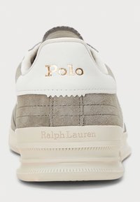 Suedefärgade grå sneakers med vita detaljer. Guld "Polo"-logotyp och texten "Ralph Lauren" på hälen, med texturerade spår på ovansidan.