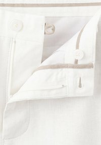 Gros plan sur la ceinture d’un pantalon blanc avec bouton, boutonnière, fermeture éclair et bordure en tissu beige contrasté.