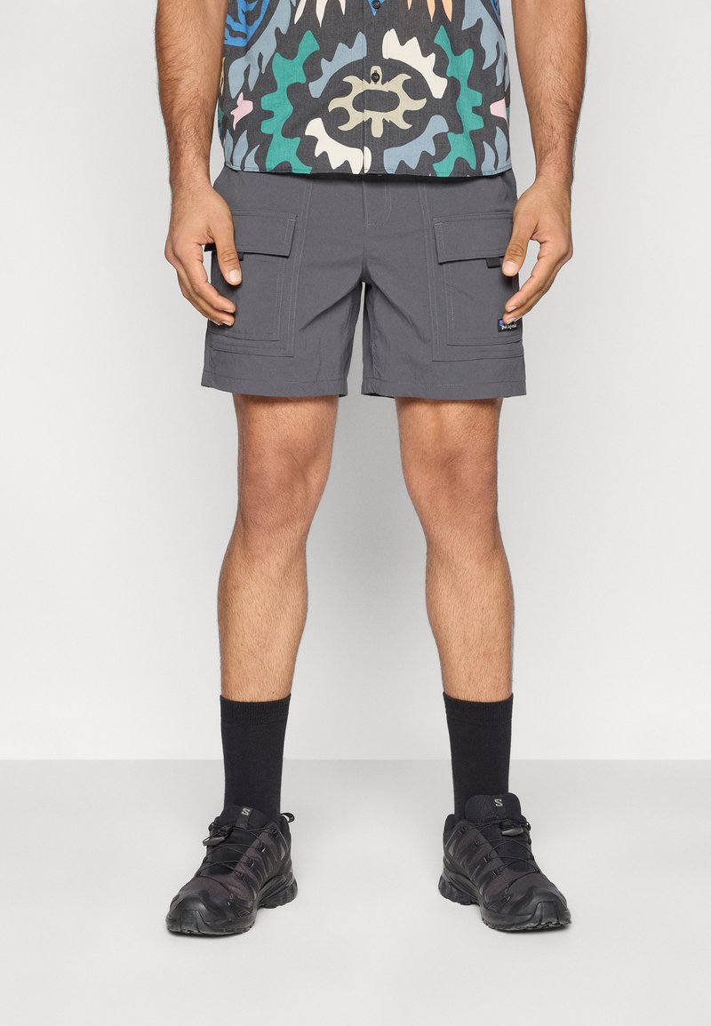 Γκρι cargo σορτς με δύο μπροστινές τσέπες, σε συνδυασμό με μαύρες κάλτσες αστραγάλου και μαύρα αθλητικά παπούτσια. Το ύφασμα φαίνεται ελαφρύ με λεία υφή.