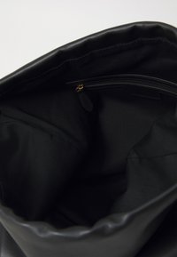 Black handbag interior showing fabric lining and a small zippered pocket with a leather pull tab.