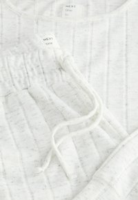 Weißes Loungewear-Set mit gerippter Textur. Das Oberteil hat einen runden Halsausschnitt; die Hose hat einen elastischen Bund und eine Kordel. Minimalistisches Design.