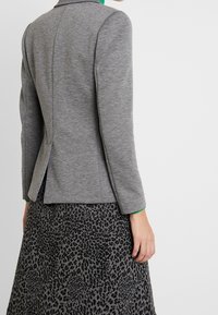 Blazer grigio a maniche lunghe, con trama sottile, forma aderente e dettaglio con spacco posteriore. Abbinato a una gonna con stampa leopardata nero e grigio.