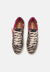 Sneakers har et svart og beige zebra mønster, med en teksturert overdel, rosa detaljer og beige snørebånd. Dekorativt hardware på siden.