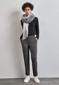 Schwarzes Langarmoberteil, grau-weiß gemusterter Schal, karierten graue Hose und weiße Sneakers mit cremefarbenen Akzenten.