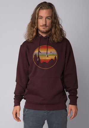 Hoodie bordeaux avec un graphisme central présentant des rayures horizontales en orange, vert et jaune, et des silhouettes d'arbres et de montagnes.
