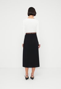 Μακρύ μαύρο φόρεμα με εφαρμοστό λευκό πάνω μέρος, που διαθέτει καφέ ζώνη στη μέση. Το φόρεμα πέφτει μέχρι τους αστραγάλους. Λείο υφή.