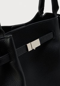 Μαύρη τσάντα χειρός από δερμάτινη υφή με διπλές λαβές και ένα ορθογώνιο ασημένιο κούμπωμα σε λουράκι από δέρμα κατά μήκος του εμπρόσθιου πάνελ.