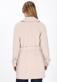 Lichtbeige jas met een brede kraag, een ceintuur in de taille en opgerolde manchetten. Zacht materiaal met een gladde textuur, rechte snit en lengte tot boven de knie.