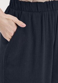 Svarta, lätta byxor med ett strukturerat tyg. Har elastisk midja och sidofickor, med en avslappnad passform.