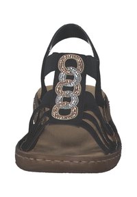 Svart sandal med flera remmar, prydd med ett dekorativt metallkedjeaccent. Brun vadderad sula, öppen tå-design. Platt sula.