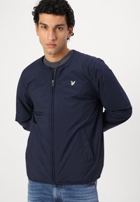 Veste bombardier bleu marine en tissu léger, dotée d'une fermeture éclair, de poches latérales et d'un petit emblème sur la poitrine.