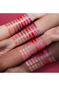 Lipstikstalen op armen tonen verschillende tinten, waaronder rood, roze en nude. Glanzende en matte afwerkingen zijn zichtbaar.