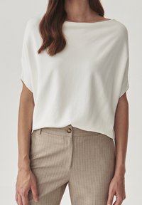 Top blanco de manga corta con escote barco combinado con pantalones de rayas finas color marrón claro que presentan un discreto botón en la cintura.