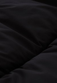 Tessuto trapuntato nero con una texture morbida, caratterizzato da sezioni lisce e gonfie che creano un aspetto accogliente.