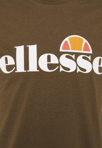 Brūna kokvilnas t-krekls ar baltu "ellesse" logotipu un krāsainu pusapļa dizainu oranžā un sarkanā krāsā virs teksta.