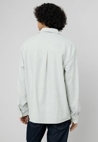 Chemise légèrement rayée blanche avec des rayures vertes et bleues ; coupe décontractée, poignets boutonnés et détail de pli dans le dos ; fabriquée en tissu texturé.