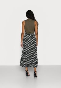 Olivgrön ärmlös topp kombinerad med en lång svartvit skärnmönstrad kjol, kompletterad med svarta ankelsandaler.