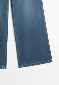 Two legs of blue denim wide-leg jeans on a white background, showing fabric texture and stitched hems.