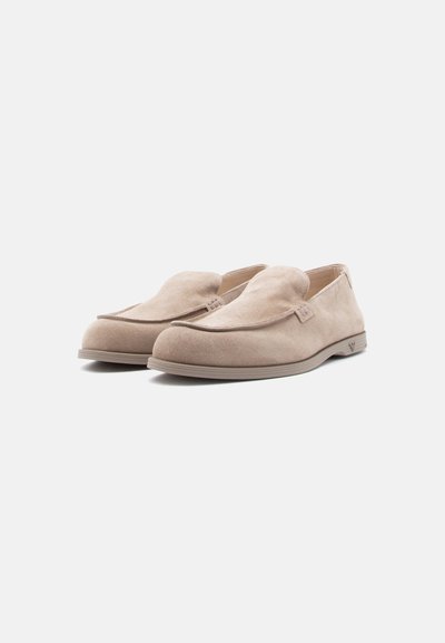 Ζευγάρι μπεζ μοκασίνια από σουέτ, με στρογγυλεμένες μύτες και χαμηλές σόλες από καουτσούκ, πάνω σε απλό λευκό φόντο.