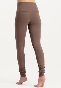 Leggings marron taille haute en matériau extensible, dotés de détails froncés au niveau des chevilles et d'une finition lisse. Pas de motifs ni de matériel visible.