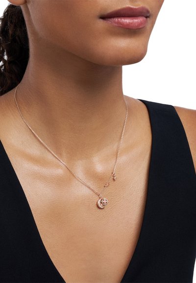 Collar de oro rosa con un charm de luna creciente y un acento de estrella, cadena delicada y detalles intrincados en el colgante, sobre un fondo de tela negra.