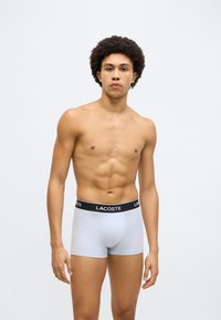 Boxer blu chiaro con elastico in vita nero con logo Lacoste. Il tessuto appare liscio, con un design aderente e cuciture minimali.
