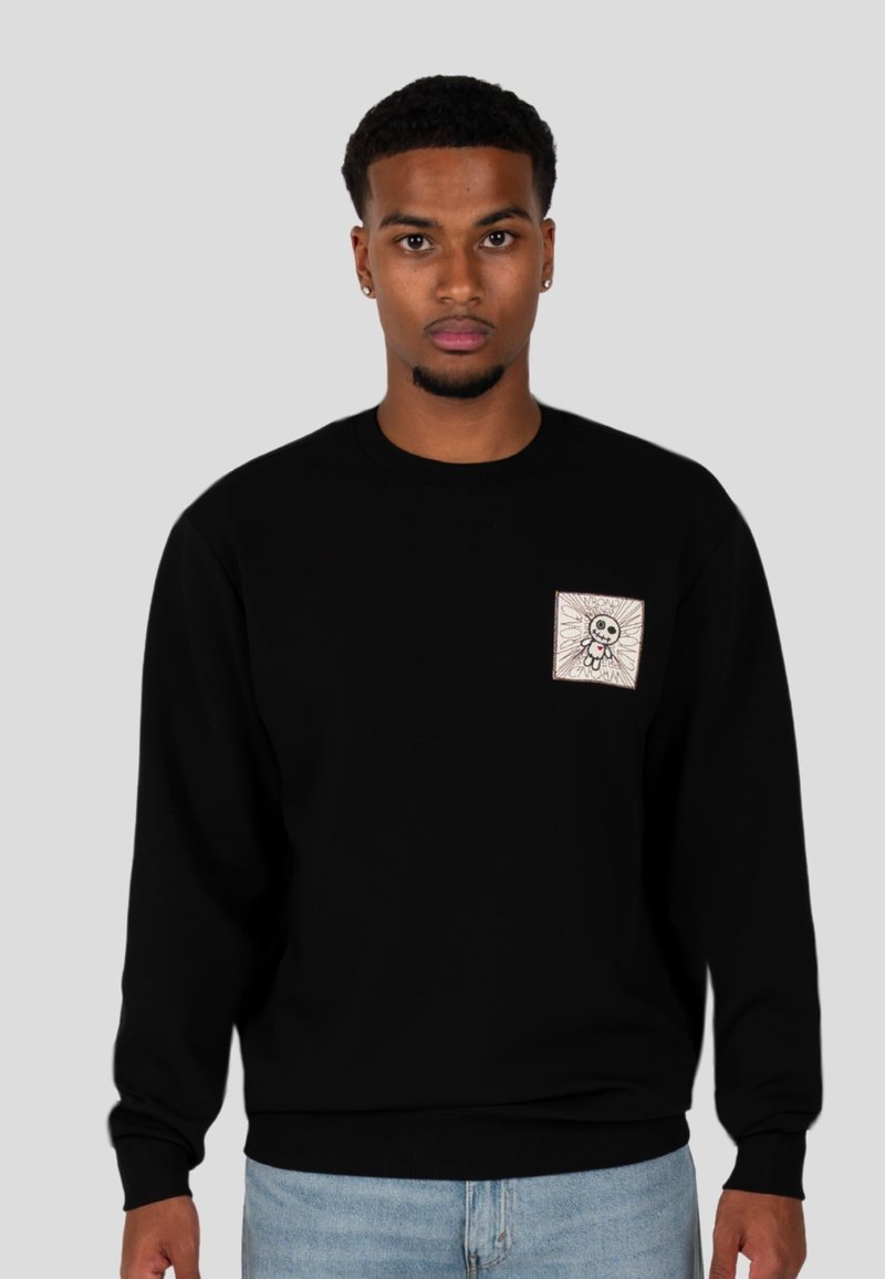 Felpa nera con un piccolo design a forma di quadrato che presenta un personaggio stilizzato. Tessuto morbido, scollatura a girocollo e polsini a coste. Vestibilità casual.