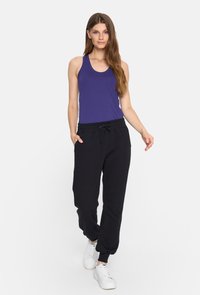 Fioletowy top na ramiączkach z okrągłym dekoltem, w zestawieniu z czarnymi spodniami dresowymi z elastycznym pasem i zwężanymi nogawkami. Białe tenisówki.