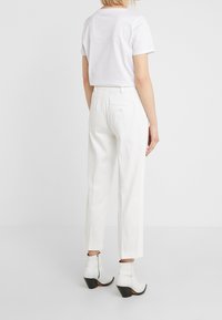 Białe spodnie o prostym kroju, zestawione z białą bluzką z krótkim rękawem. Całość dopełniają białe botki za kostkę na słupku.