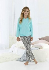 Világoskék hosszú ujjú V-nyakú felső fekete-fehér mintás pizsamanadrággal. A modell mezítláb áll, lágy háttér előtt.