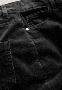 Pantaloni din catifea neagră cu textură ribbed vizibilă, o buză de spate și un detaliu din metal lângă talie.