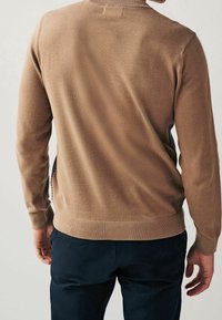 Brauner, gestrickter Pullover mit einem runden Ausschnitt, gerippten Bündchen und kontrastierenden Seitenpaneelen. Weiche Textur, körpernahe Passform, minimale Details.