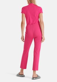 Combinaison fuchsia à manches courtes, taille cintrée et pantalon droit. Portée avec des chaussures à enfiler rayées noir et blanc.