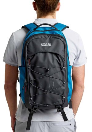 Un hombre visto desde atrás lleva una mochila negra y azul con cordones elásticos en la parte delantera, compartimentos con cremallera y correas ajustables.
