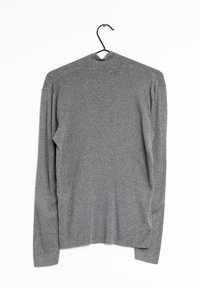 Chemise grise à manches longues en tissu doux et texturé. Présente un col haut et une coupe décontractée avec un minimum de détails. Accrochée à un crochet.