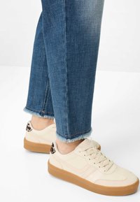 Crèmekleurige sneakers met een suède zool, voorzien van een vetersluiting en luipaardprint accenten op de hiel. Gecombineerd met blauwe jeans met rafelige zoom.