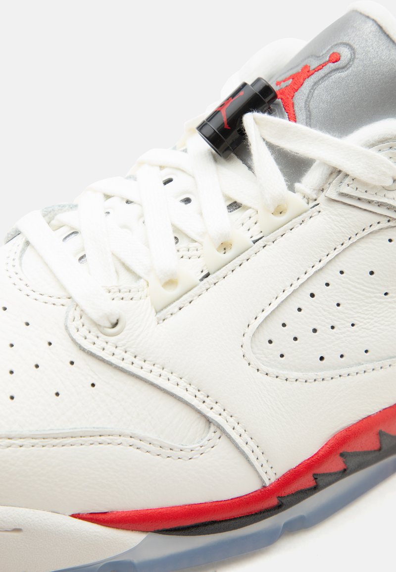 Zapatilla de cuero blanca y gris con cordones blancos, detalles en rojo y negro en la suela, y un logo Jumpman rojo en la lengüeta gris.