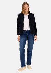 Granatowa polarowa kurtka z zamkiem z przodu i bocznymi kieszeniami, zestawiona z niebieskimi dżinsami i beżowymi trampkami, prezentująca się na jednolitym tle.