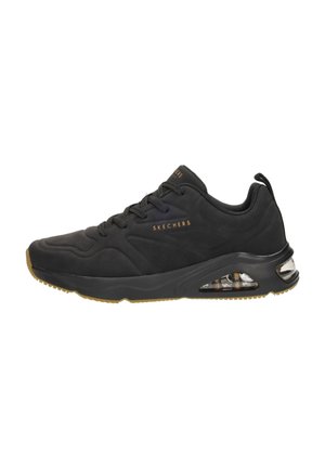 Zapatillas deportivas negras con parte superior sintética suave, acentos texturizados y amortiguación de aire visible en el talón. Suela de goma con patrón de agarre.