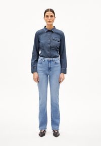 Dunkelblaue Jeanshemd mit langen Ärmeln und einer Brusttasche, kombiniert mit hellblauen geraden Jeans und schwarzen flachen Schuhen.