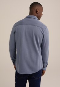Lange mouwen shirt van lichtblauwe stof met een gladde textuur, met een kraag, achterbale en knoopmanchetten. Gecombineerd met donkerblauwe spijkerbroek.