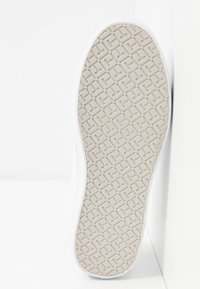 Sole of white sneaker with beige rubber outsole featuring a repeating geometric grid pattern for traction.