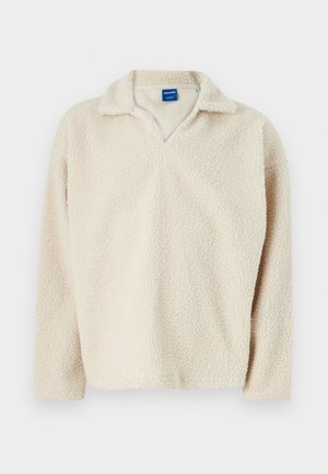 Pullover beige in pile con superficie textured e accogliente, con scollo a V e maniche lunghe. Etichetta visibile all'interno del colletto.