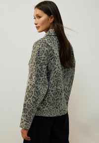 Grå denimjacka med leopardtryck i en något oversized passform. Har två bröstfickor och en klassisk krage.